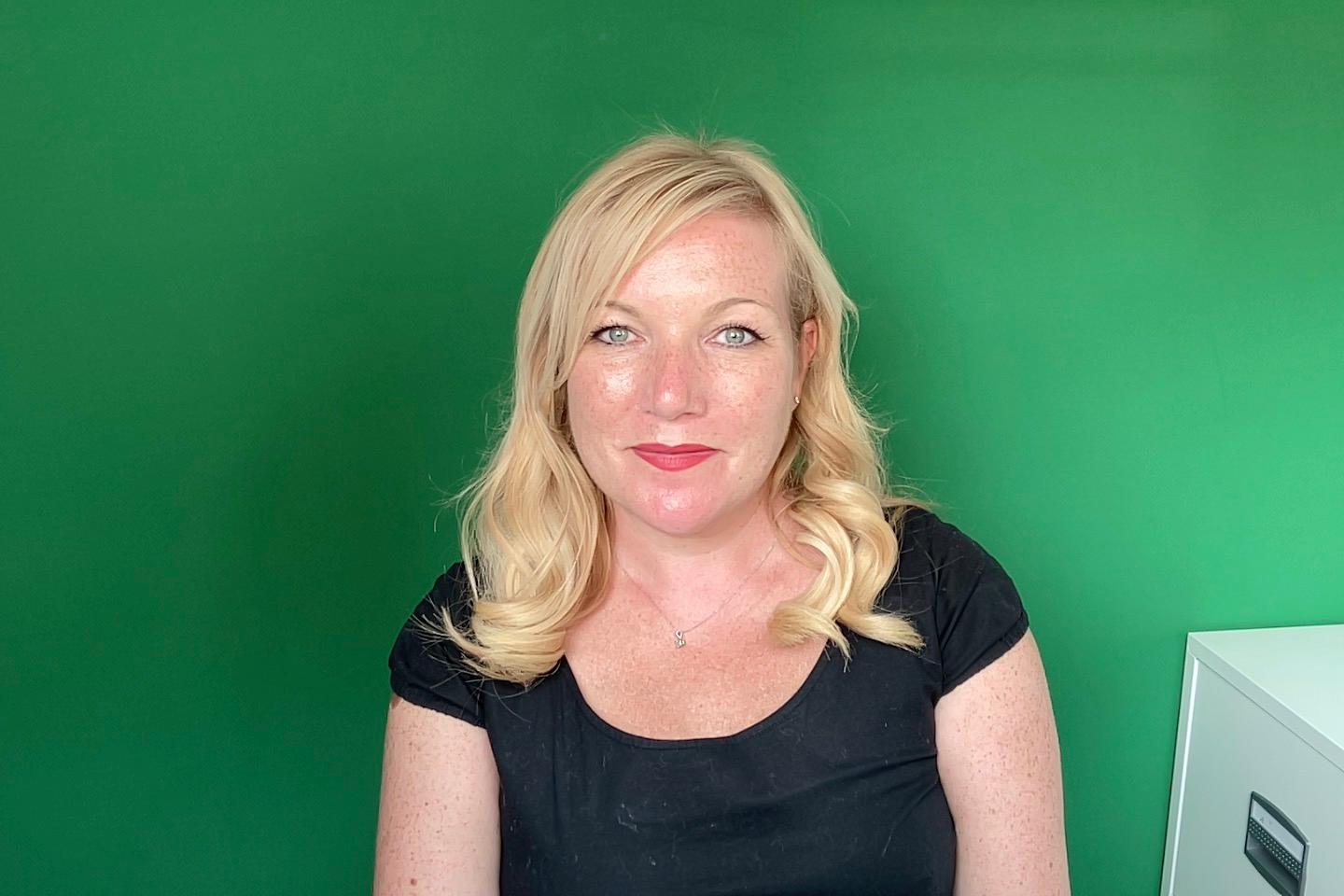A photo of Kim-Adele Randall, an alternative business coach, in front of a green screen