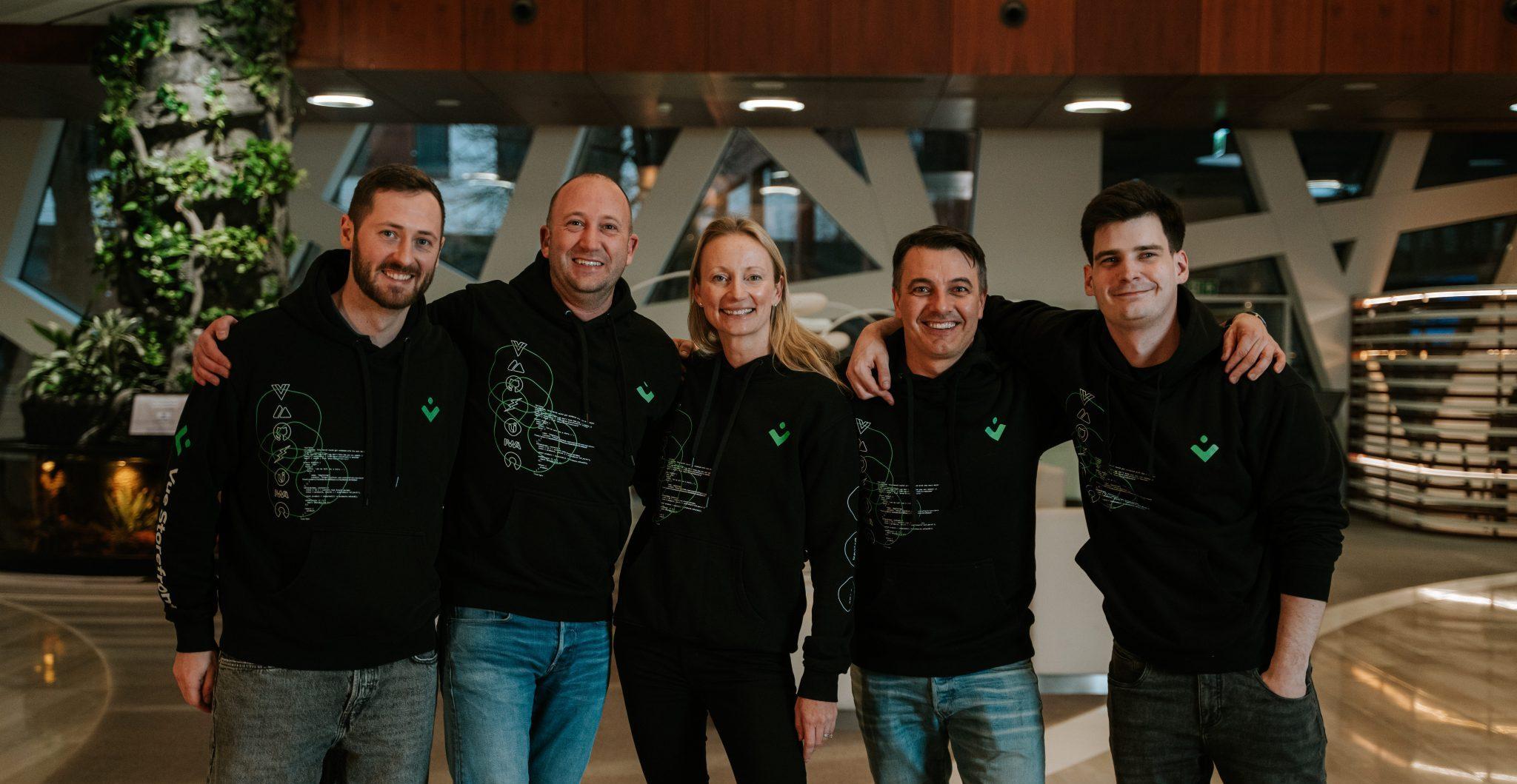 Five people standing together, with arms around their shoulders. Four men and one woman in the middle
