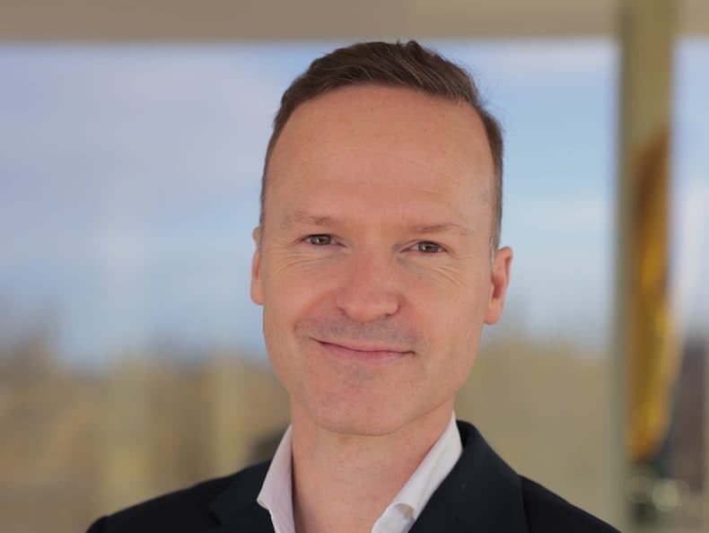 A headshot of Reinhard Meier, who is smiling at the camera against a blurred background