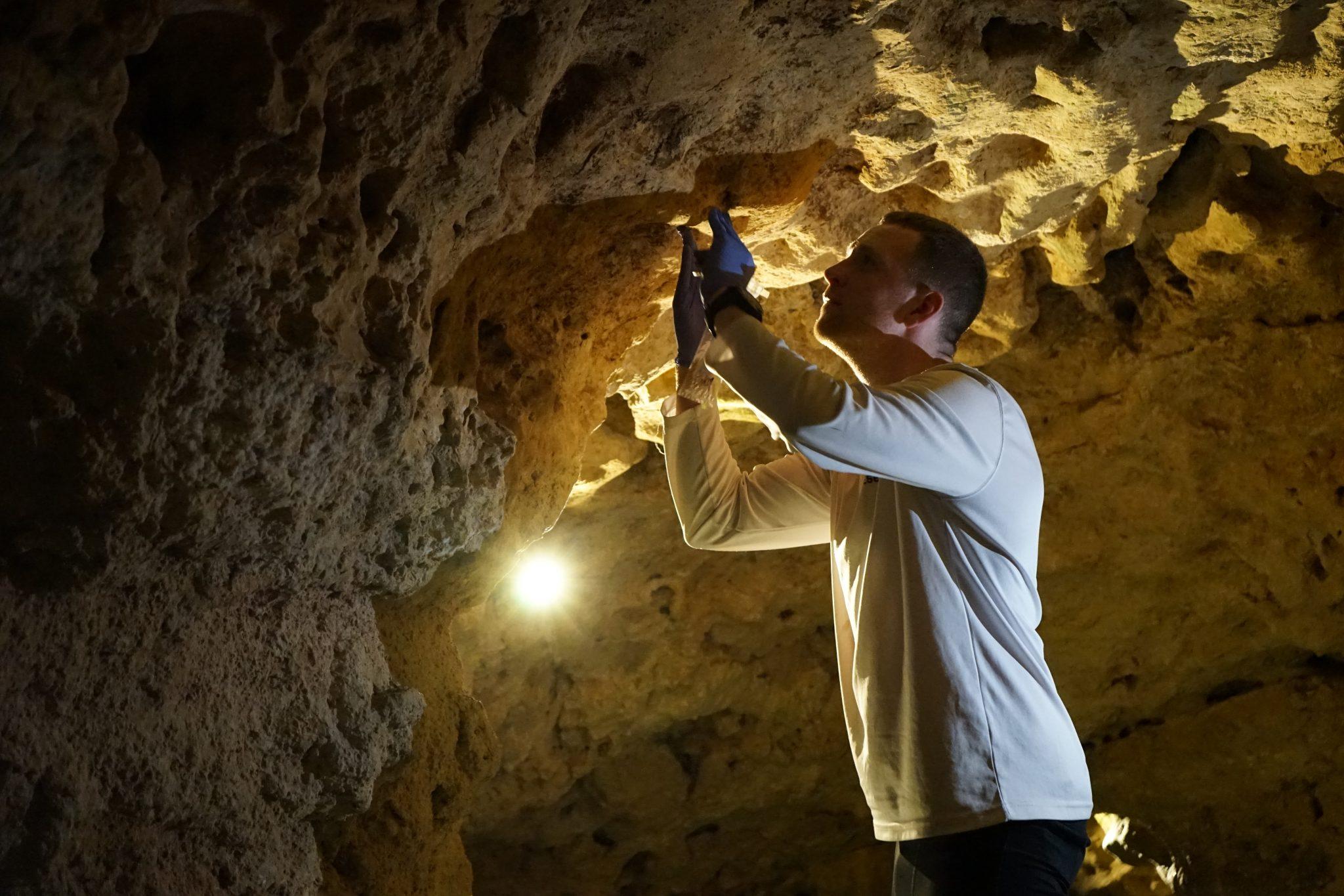 A light shines on Basecamp's Clark as he inspects a substance on the cave ceiling in Hungary.
