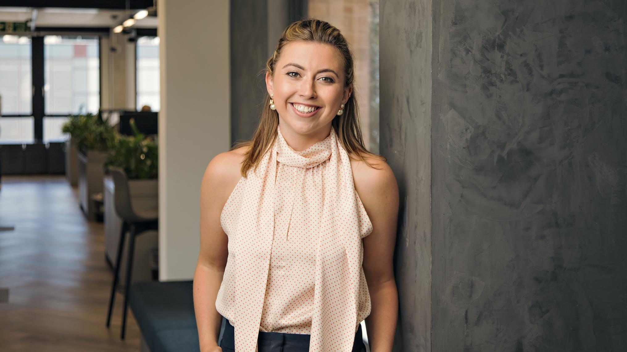 A headshot of Molly Gilmartin, who is smiling at the camera and standing in an office