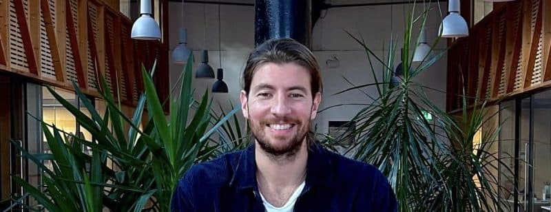 A headshot of Thanasis Mandaltsis. In the background is a room with wooden panels and plants.