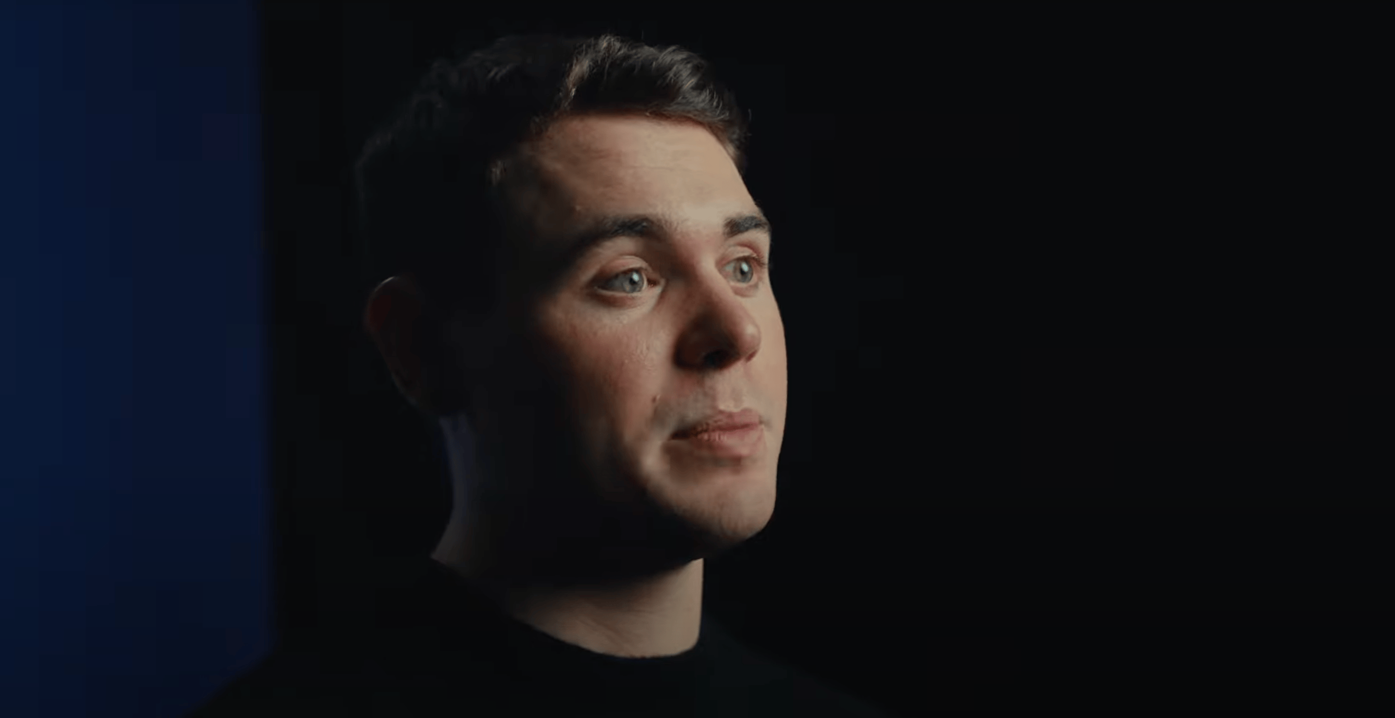 Image of James Dacombe looking away from the camera in front of a dark background.