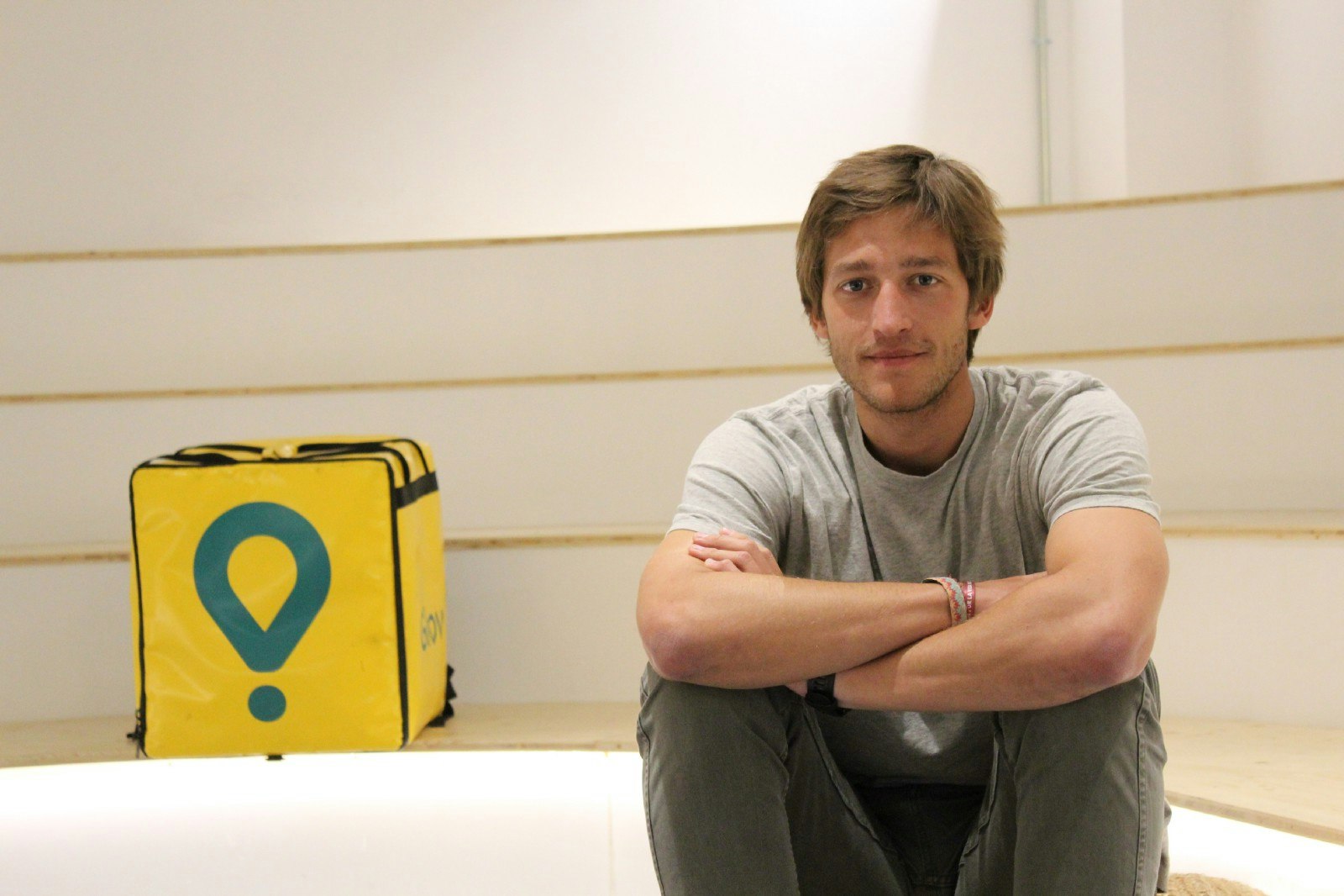 Glovo founder Oscar Pierre sitting on a set of stairs next to a Glovo delivery bag.
