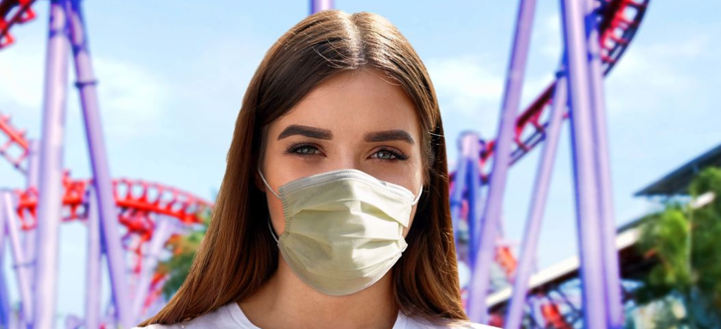 Girl wearing a mask in front of a roller-coaster