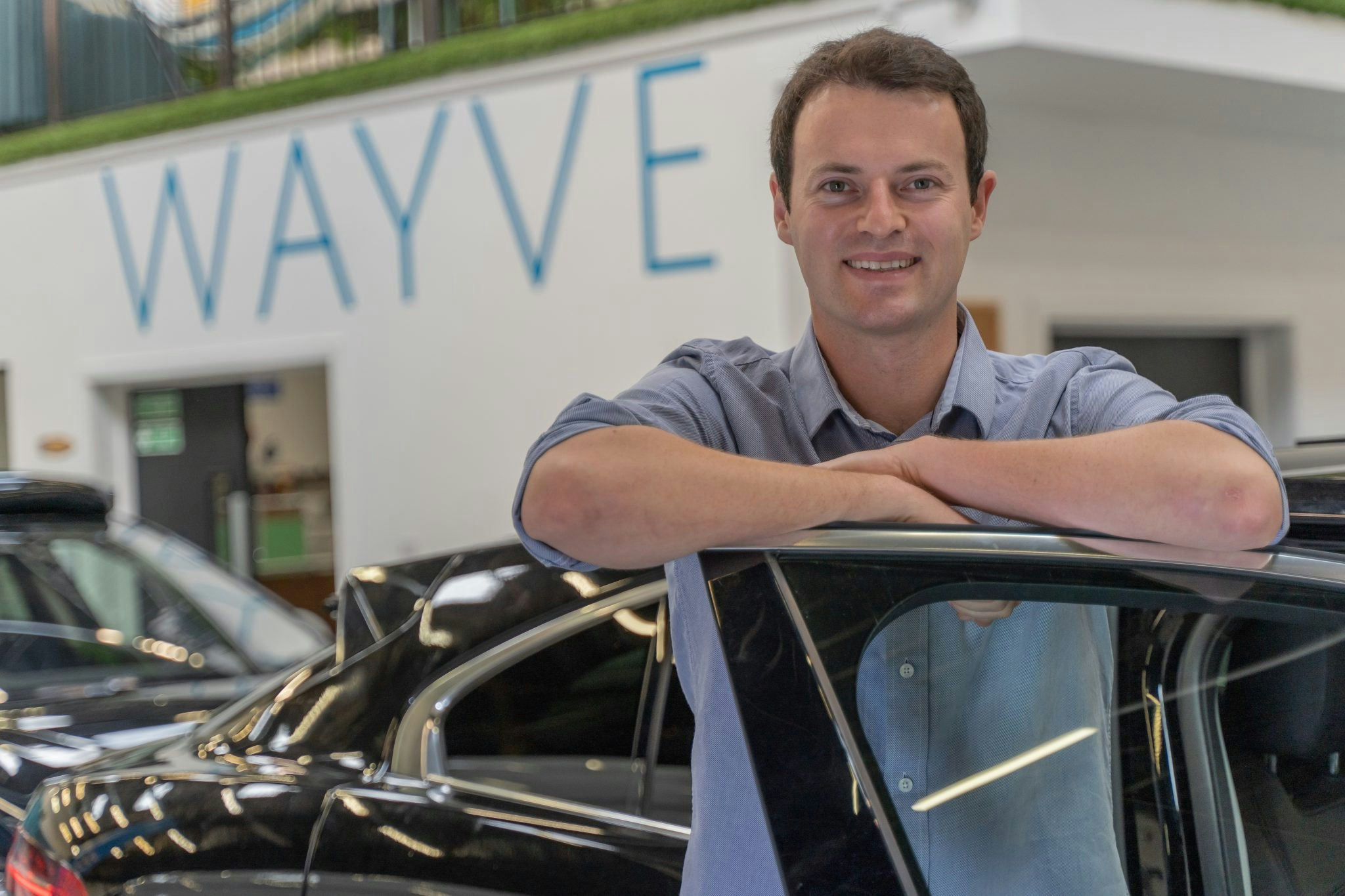 An image of Alex Kendall, CEO of Wayve, leaning against at car door.