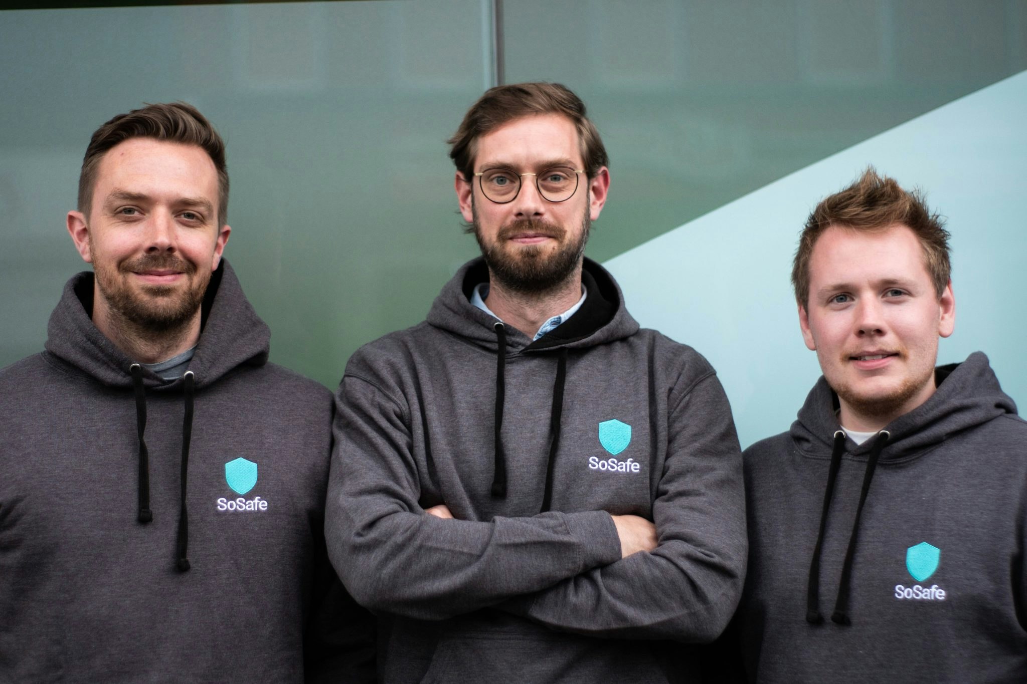 A landscape photo of three male cofounders of SoSafe in grey branded hoodies: Lukas Schaefer, Dr. Niklas Hellemann and Felix Schuerholz