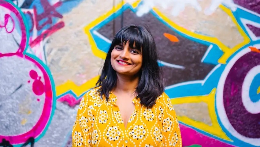 A landscape photo of Anshu Ahuja, cofounder of DabbaDrop, stood against a colourful graffiti wall.