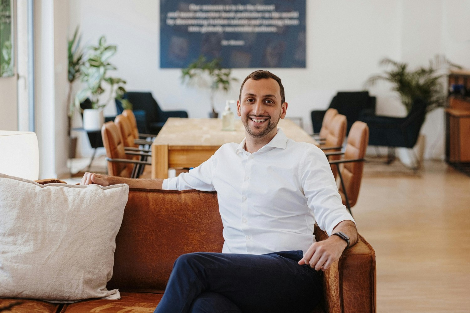 A landscape photo of Ali Abazaz sitting on a brown sofa in an office. 