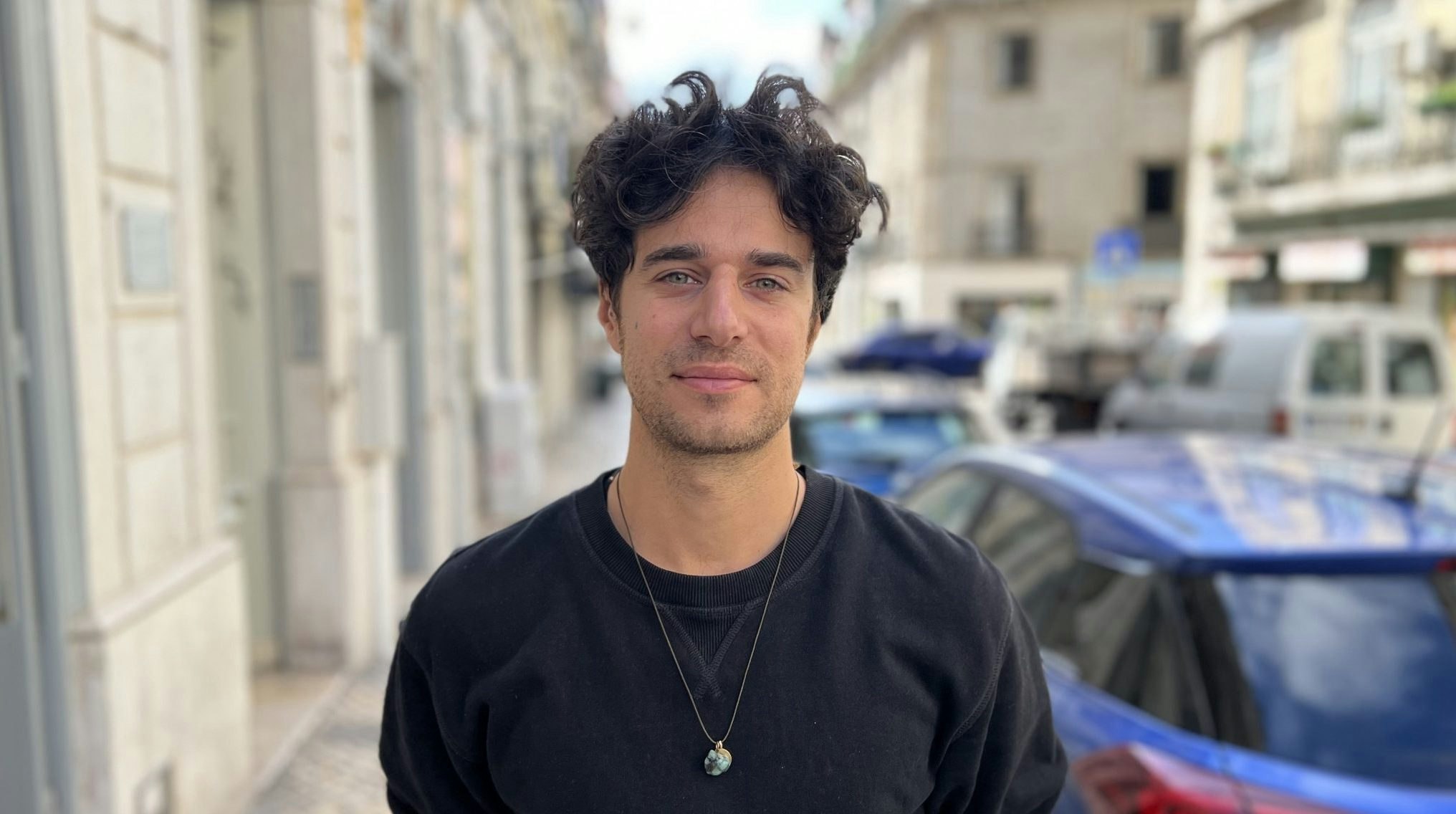 Landscape photo of Hugo Amsellem stood on a street with buildings and a car behind him.