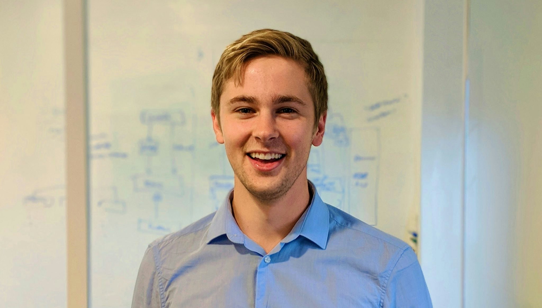 A landscape photo of Bertie Highmore smiling, wearing a blue shirt 