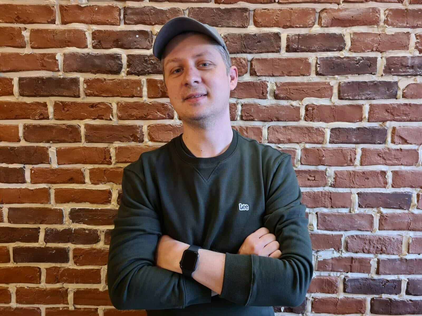 A man in a cap standing against a brick wall