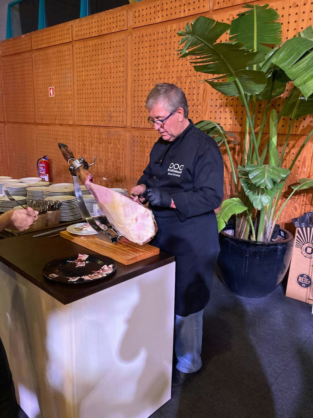 A photo of a man in all black slicing a leg of iberico ham