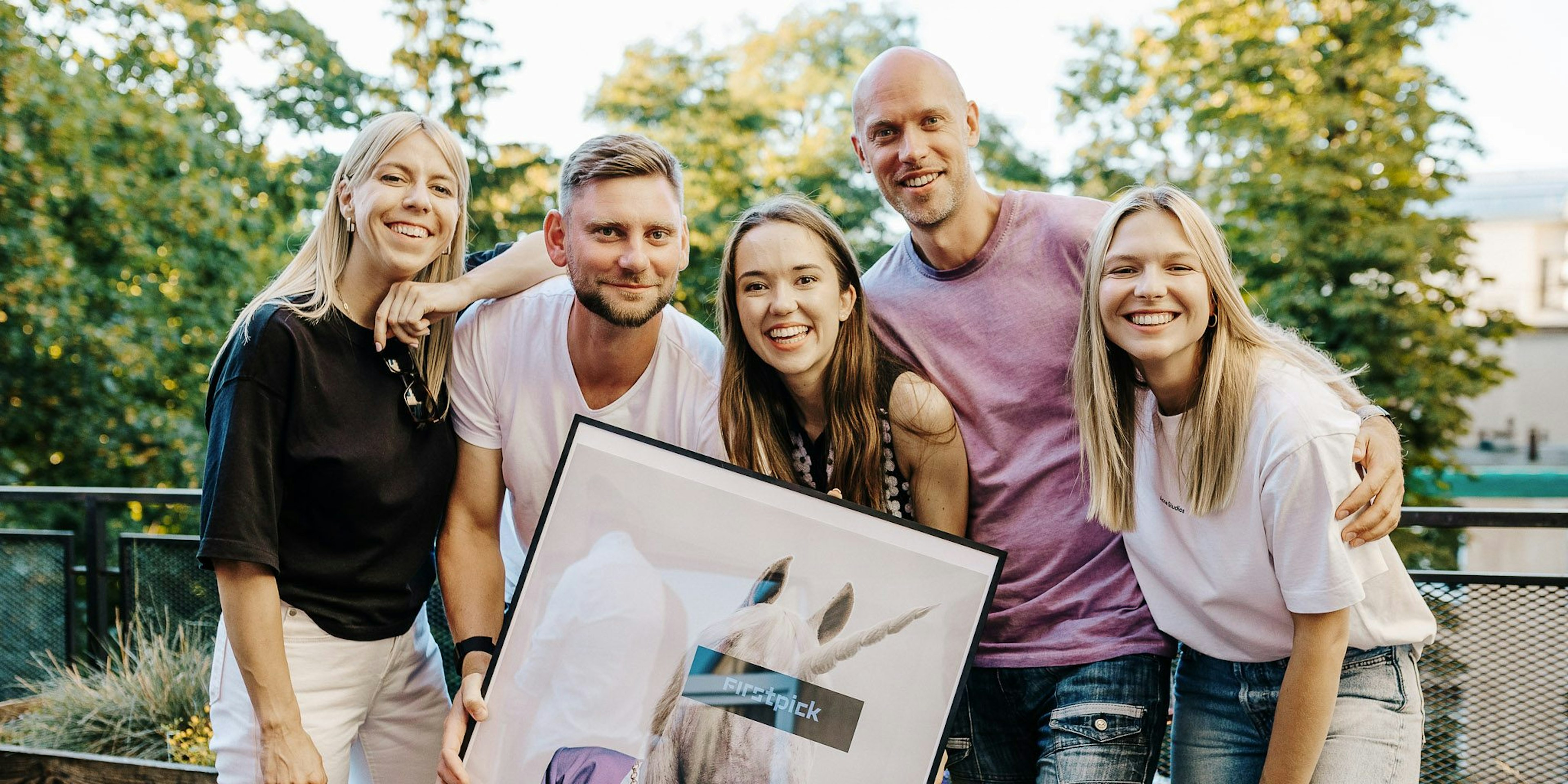 A group of five members of FIRSTPICK's team holding the picture of a unicorn