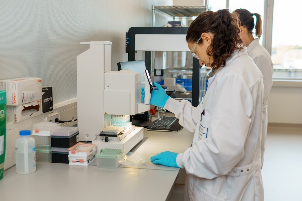 Two scientists in lab coats operating a countertop machine in a lab