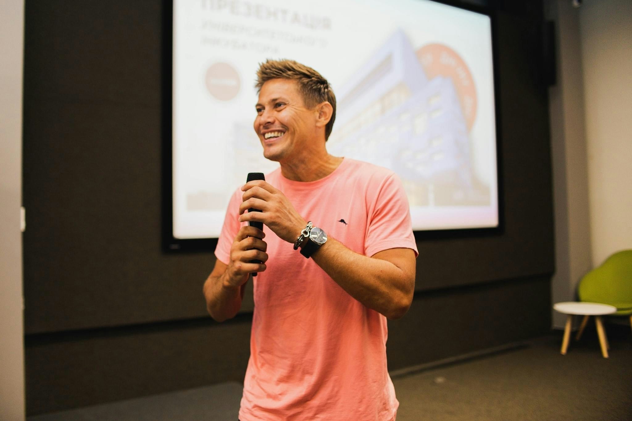 A landscape photo of Ivan Petrenko in a pink tshirt holding a microphone