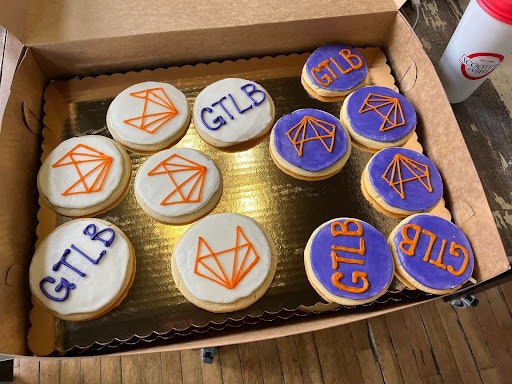 A box of cupcakes with the GitLab logo on purple and white icing 