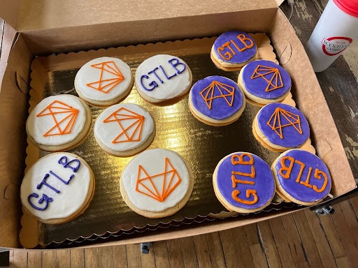A box of cupcakes with the GitLab logo on purple and white icing