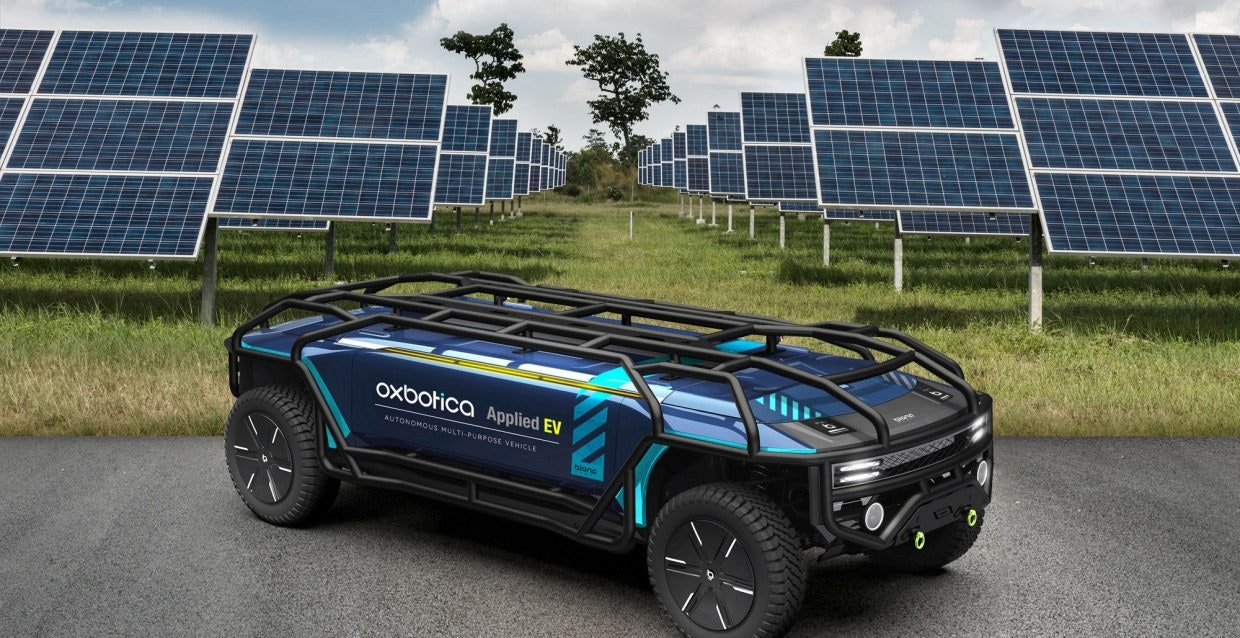 Oxbotica's AppliedEV autonomous electric vehicle, a small electric car, in front of a field with solar panels on
