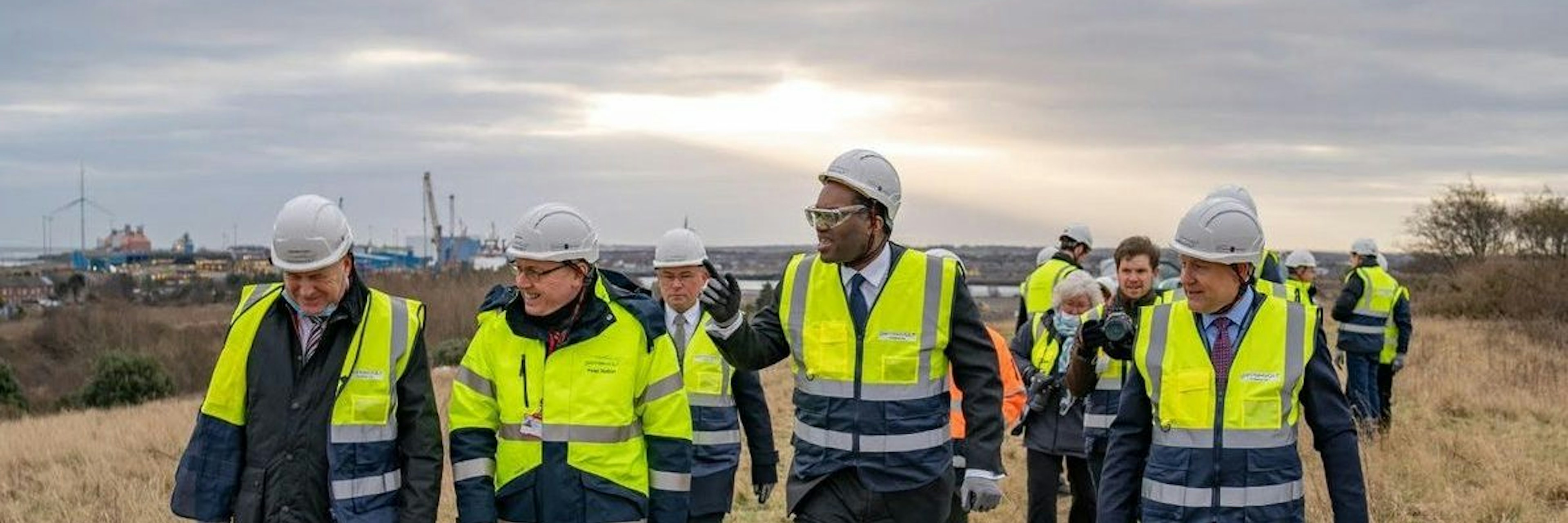 Four men in high-vis jackets and hard hats, including Britishvolt founder Orral Nadjari and former UK chancellor Kwasi Kwarteng, walk along a grassy ridge
