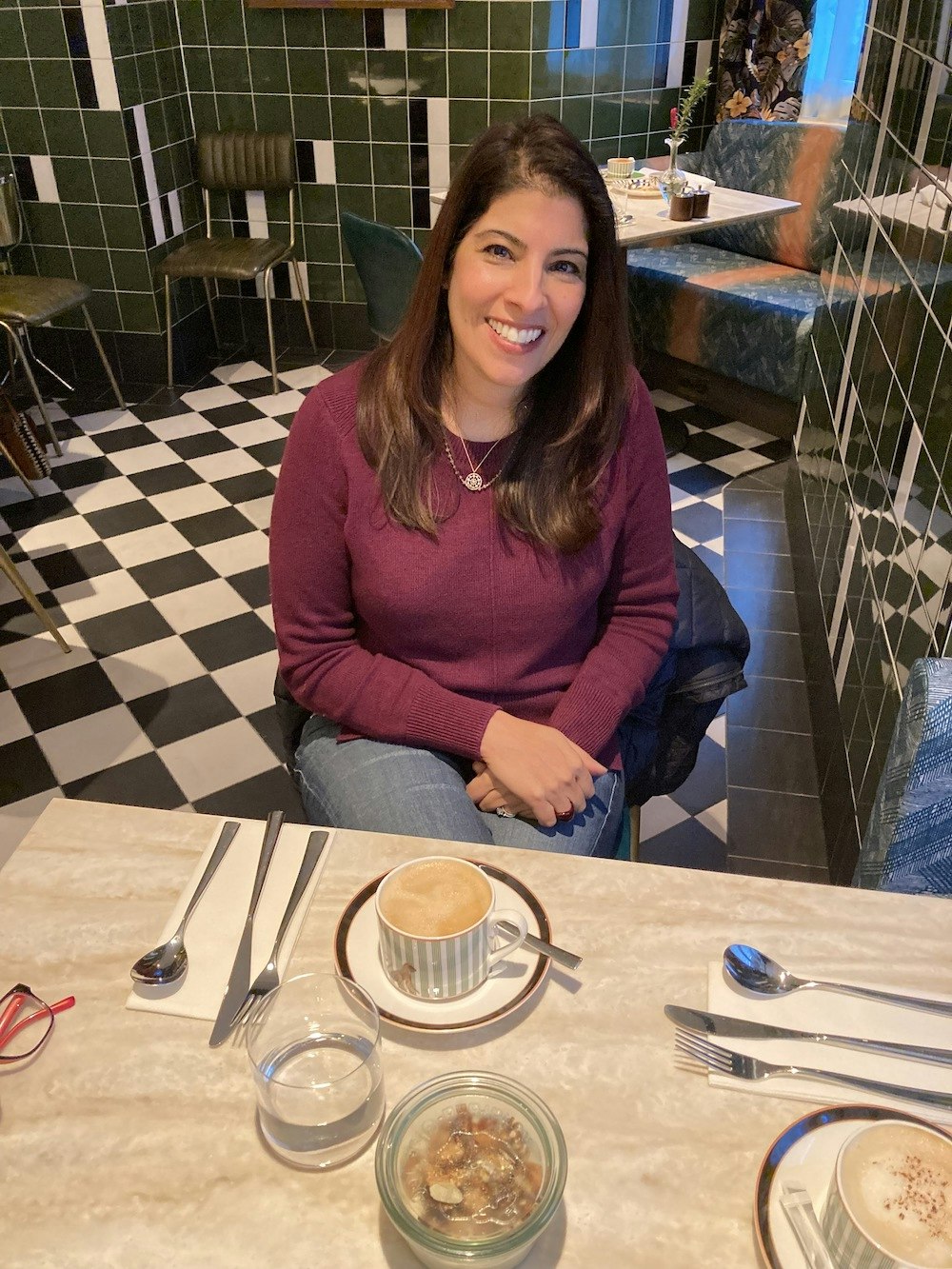 Sujata Bhatia sitting at a cafe table with a coffee and oats in front of her