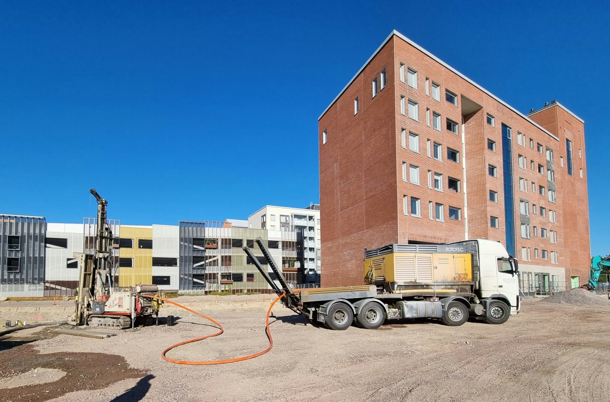 An image of a truck helping to install a ground-source heating system next to a new-build six-storey block of flats 