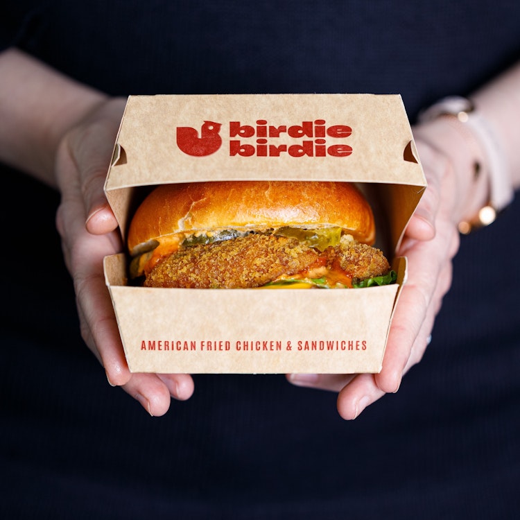 An image of a birdie birdie fried chicken burger in a cardboard container