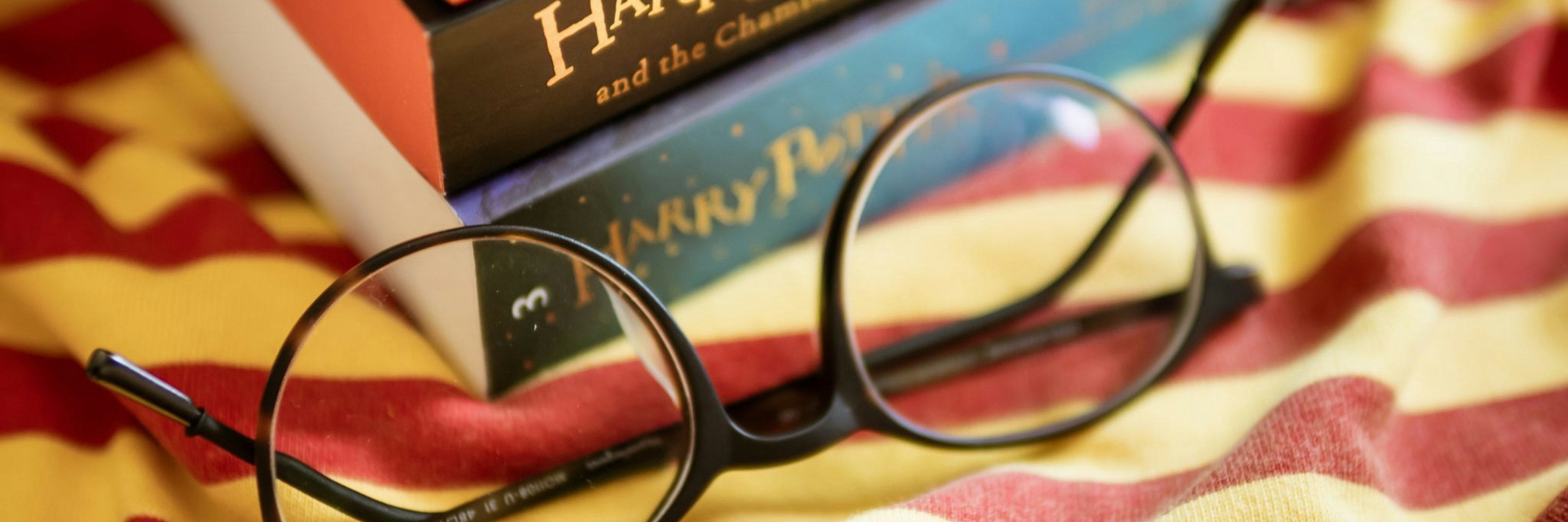 A stack of harry potter books on a red and yellow striped cloth with a pair of round glasses