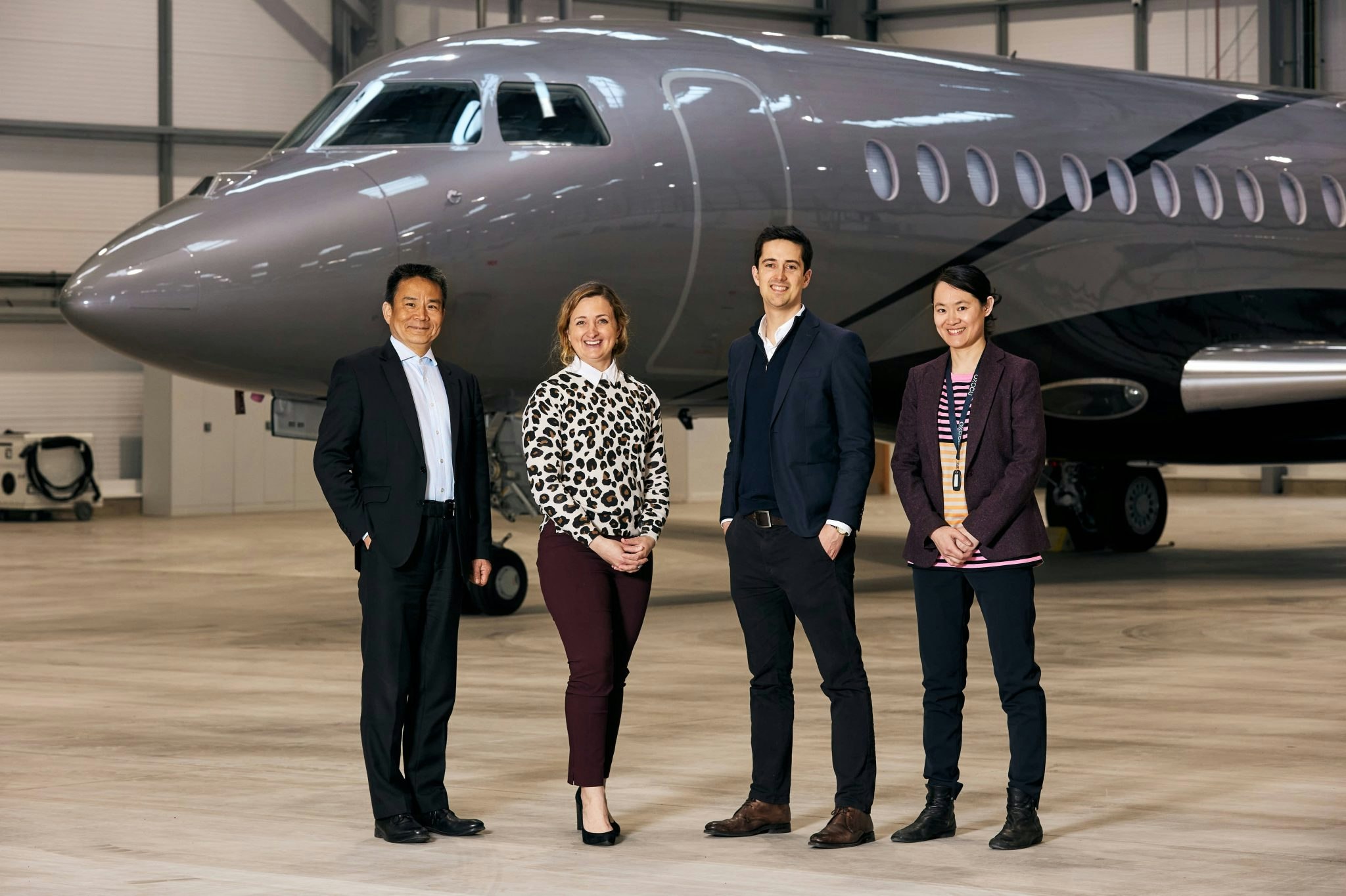 A landscape photo of four people standing in front of a grey private jet in a hangar