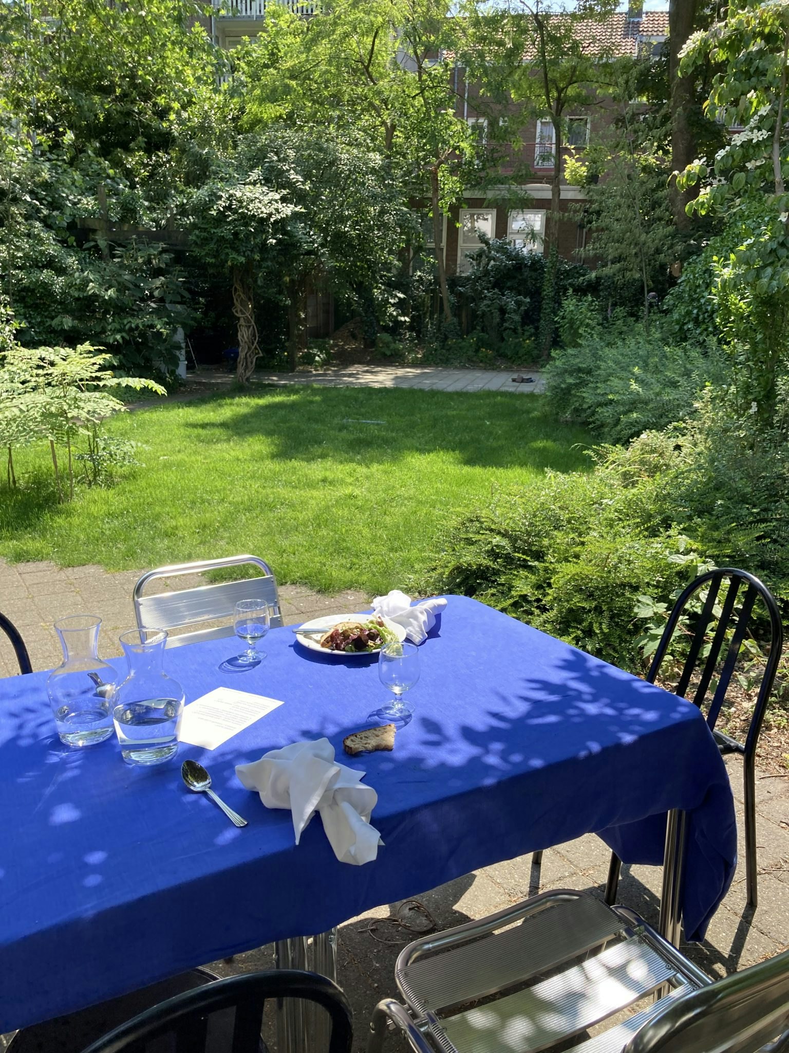 A rectangular table with a royal blue table cloth in a sunny back garden