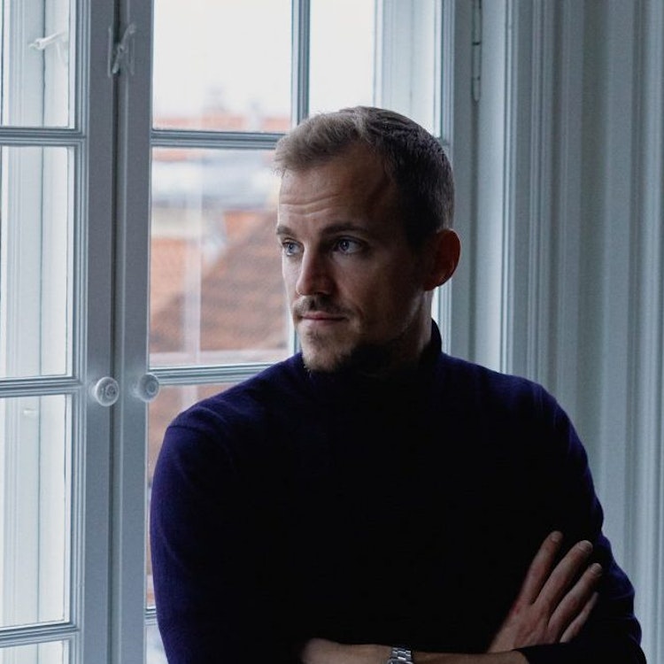 Lars Maaloe, cofounder of Corti, standing near a window with houses visible in the background.