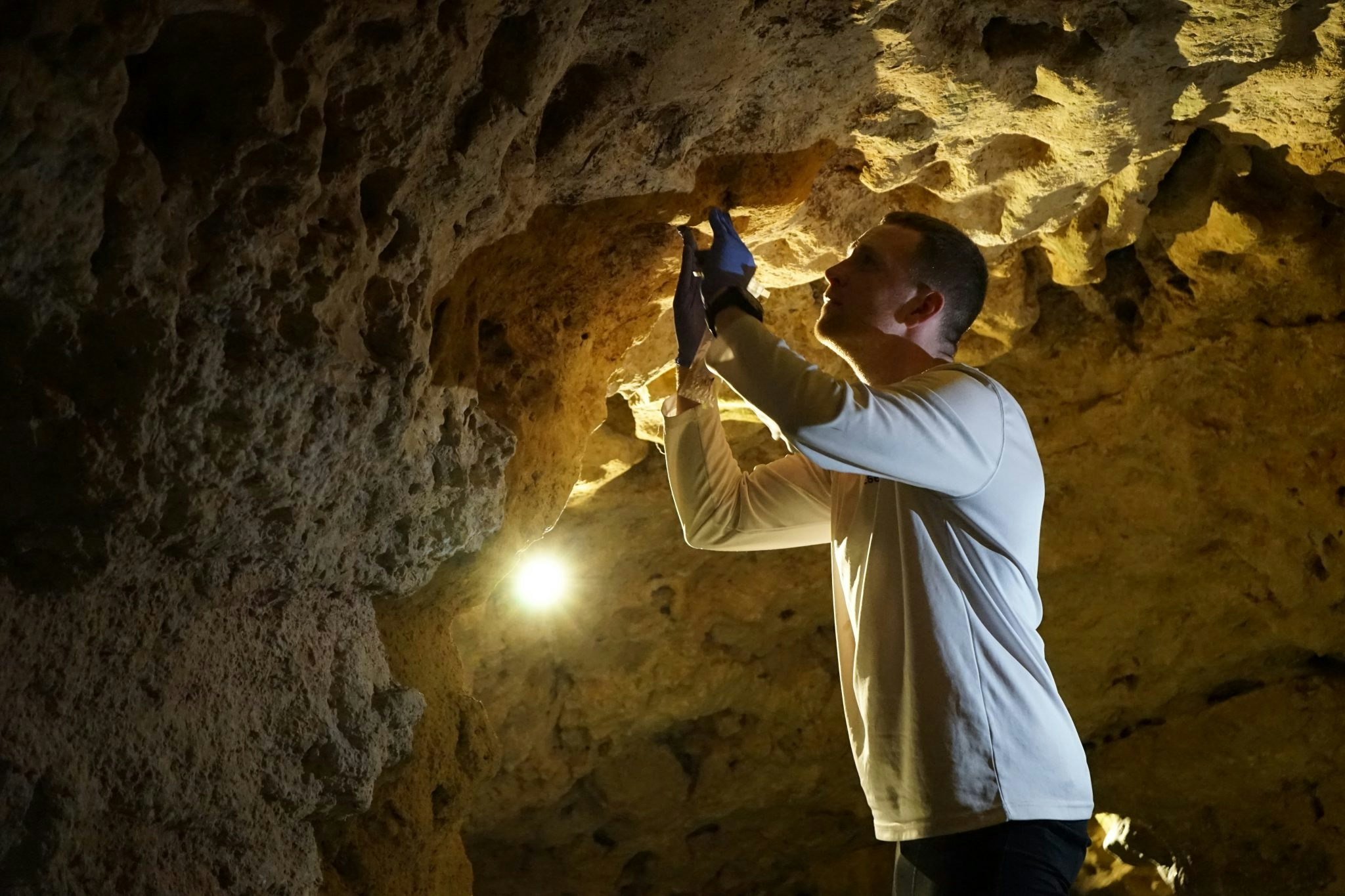 A light shines on Basecamp's Clark as he inspects a substance on the cave ceiling in Hungary.