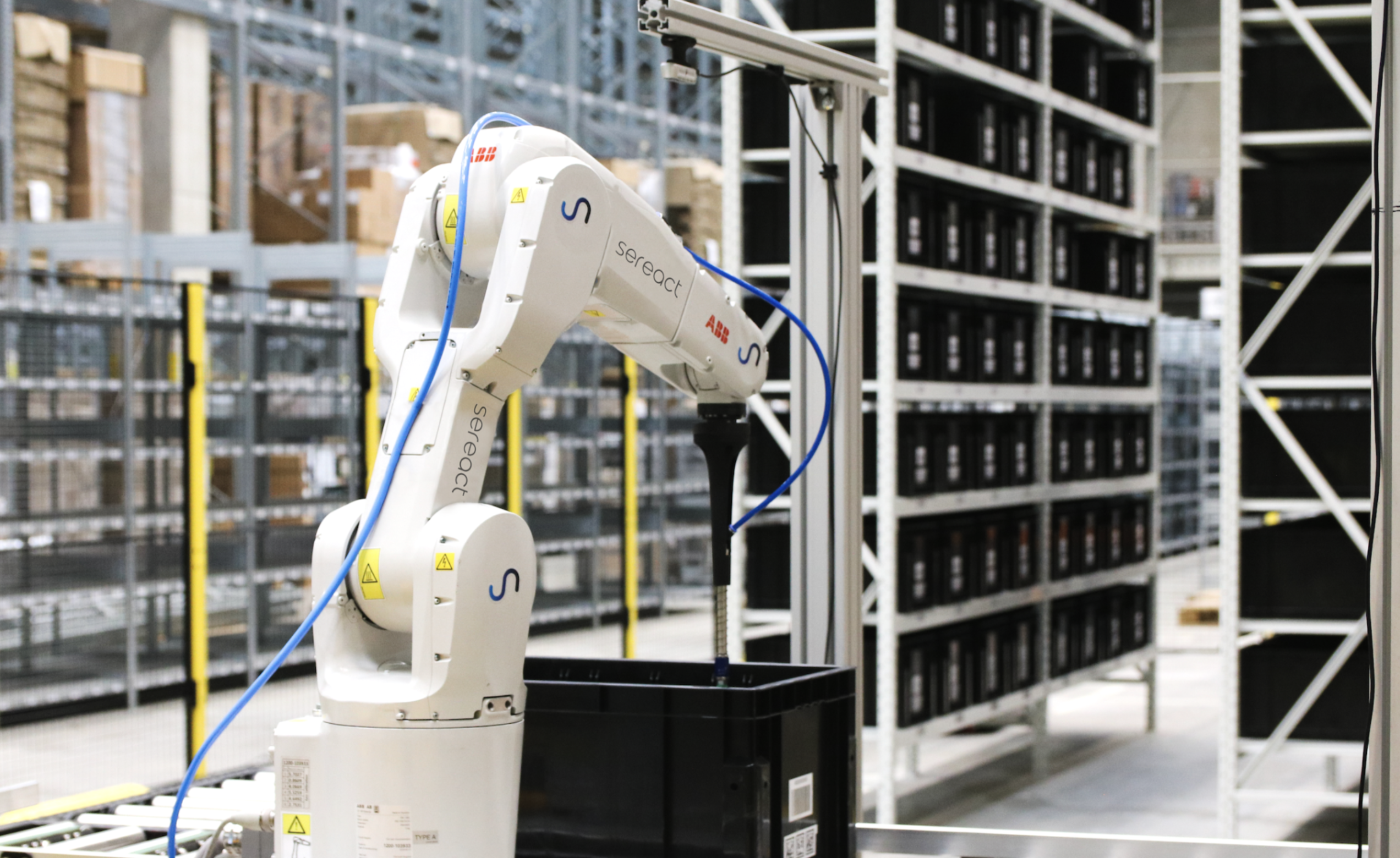 An image of an arm-like robot interacting with a plastic crate in a warehouse