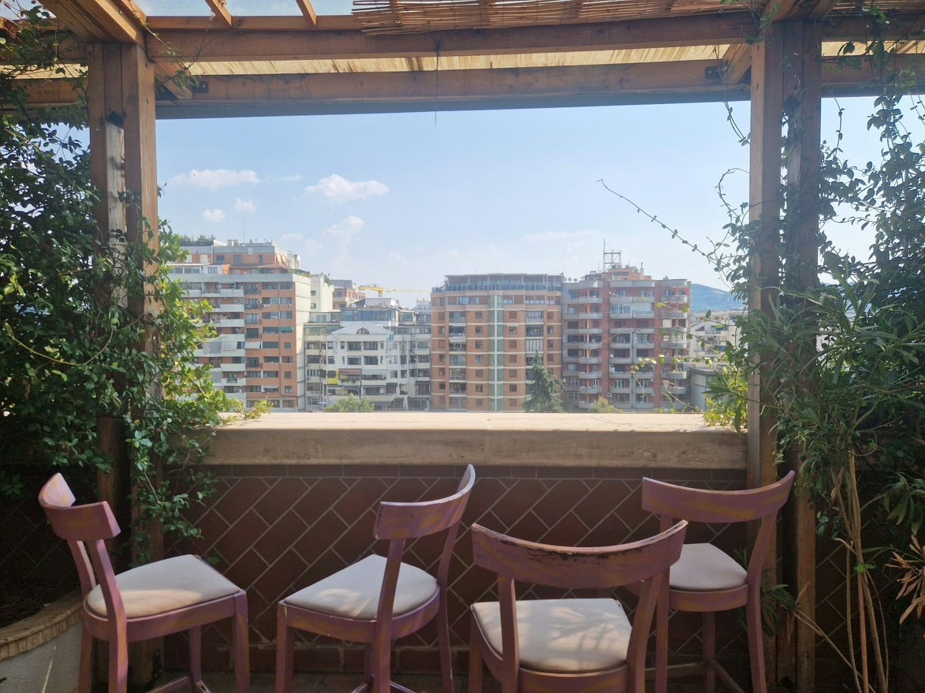 Four chairs on a balcony overlooking a city. Plants are on either side.