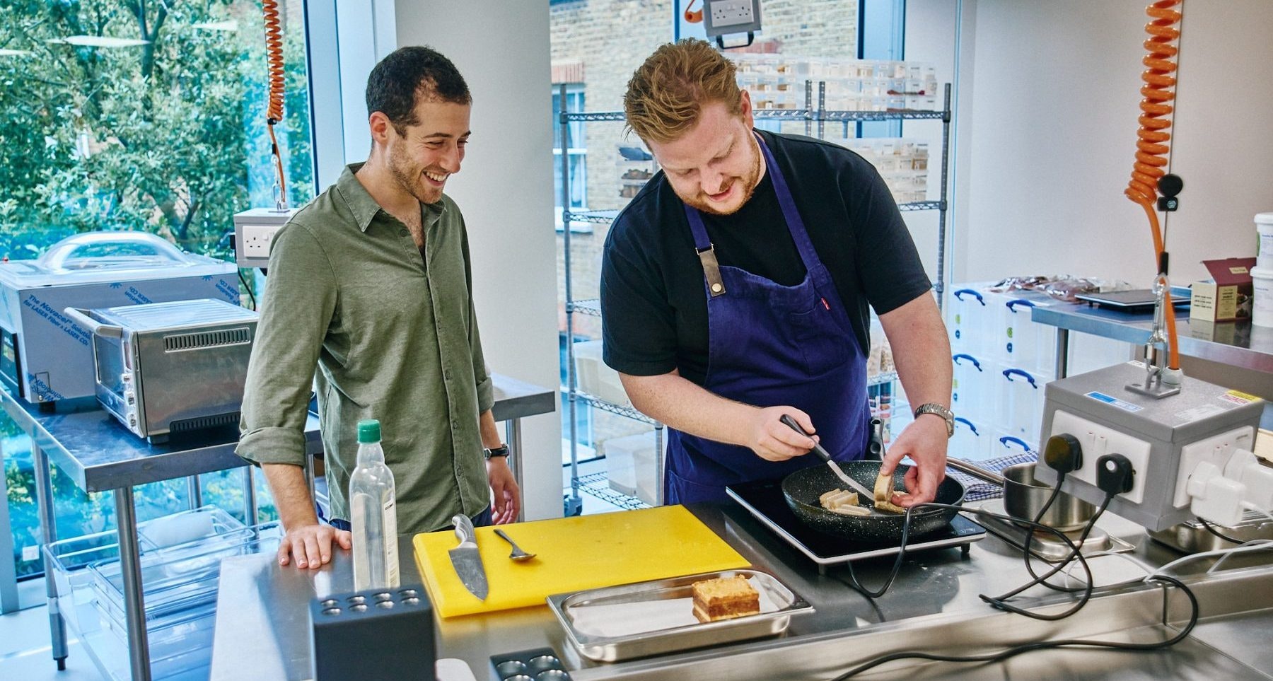 Hoxton Farms' kitchen, with two men cooking plant-based meat on a pan