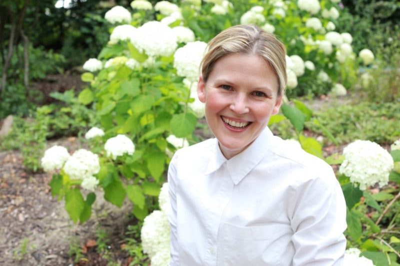 A headshot of Julia Hawkins, smiling at the camera while standing in a garden