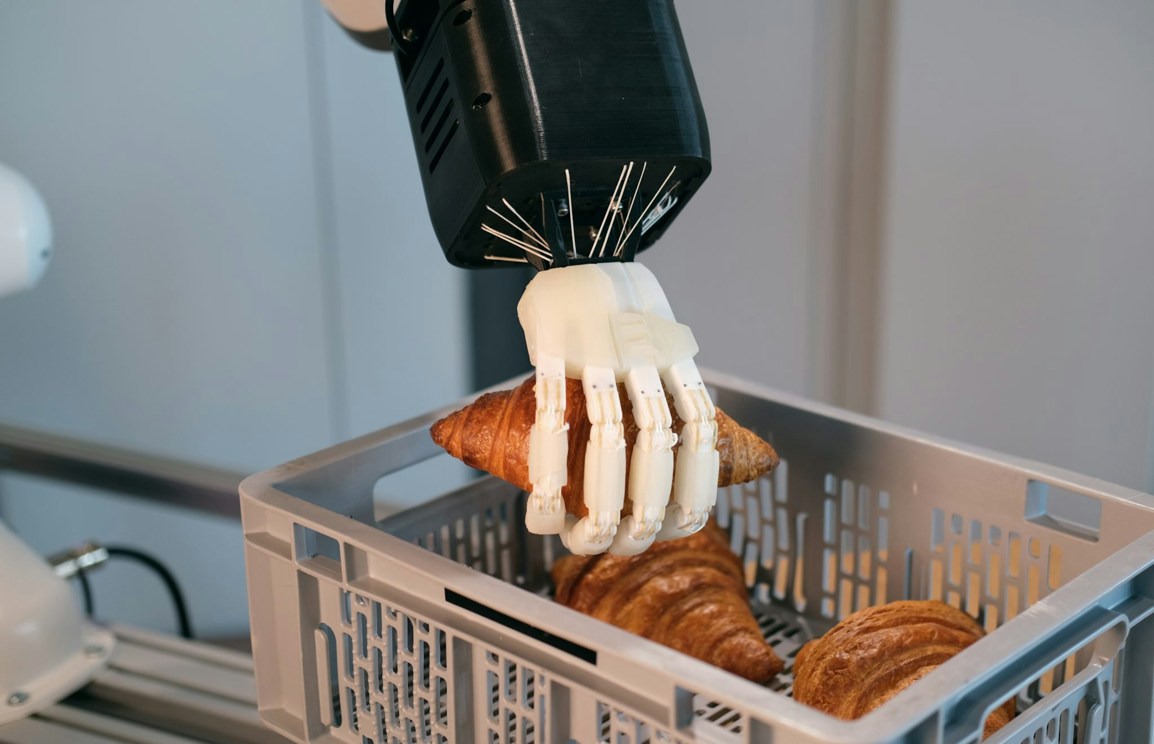 A robotic hand picking up a croissant from a basket.