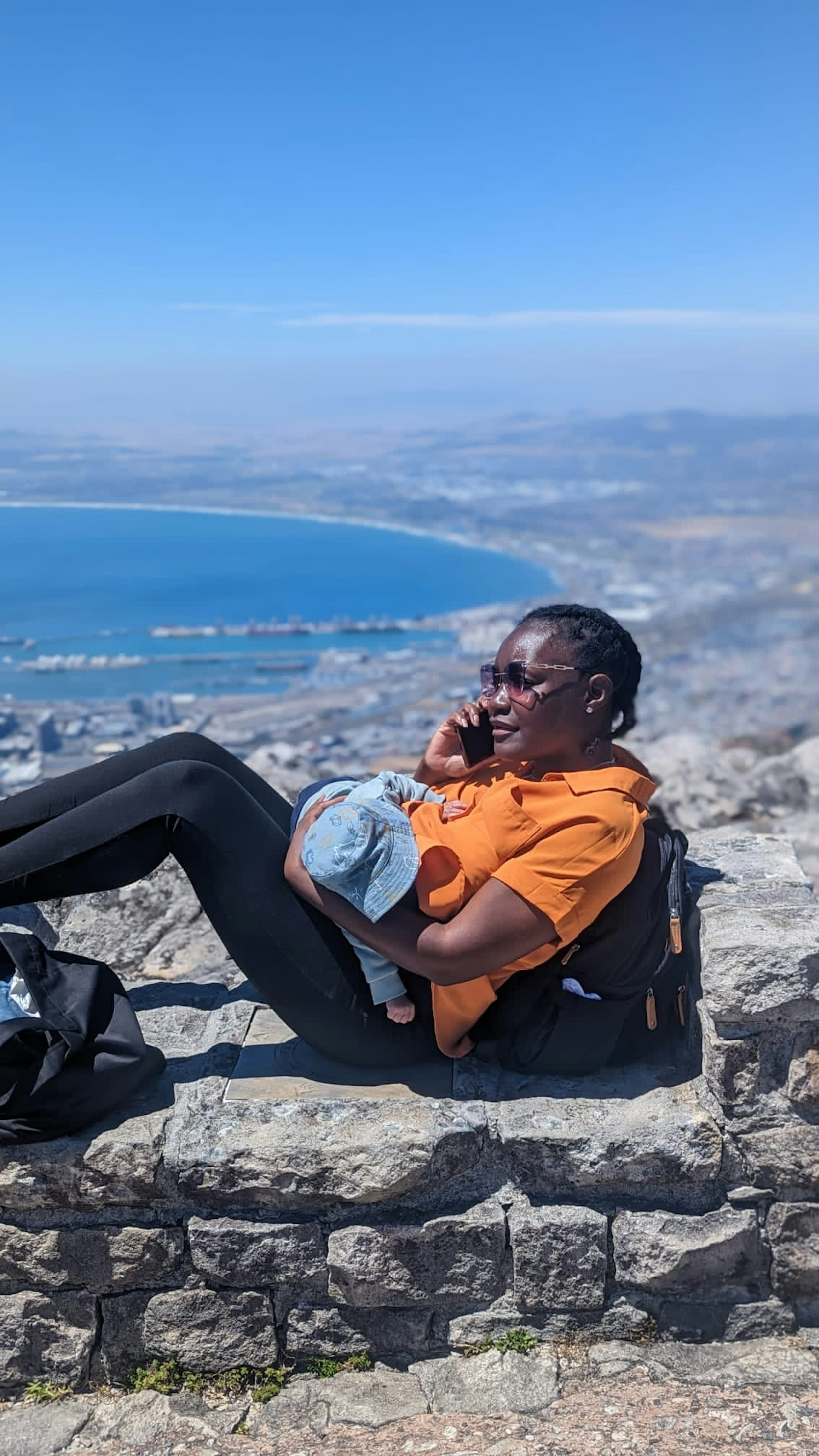 Claudine sitting in a rock on Table Mountain with her baby, taking a call 